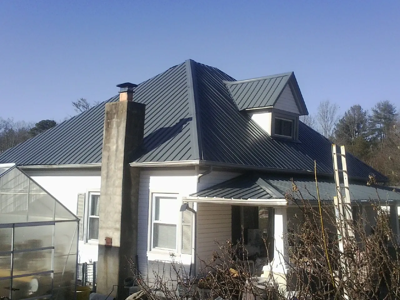 Dark blue standing seam metal roof on a white farmhouse with dormer — Slate & Tile Roof Repair by Roofing Brothers in Brick