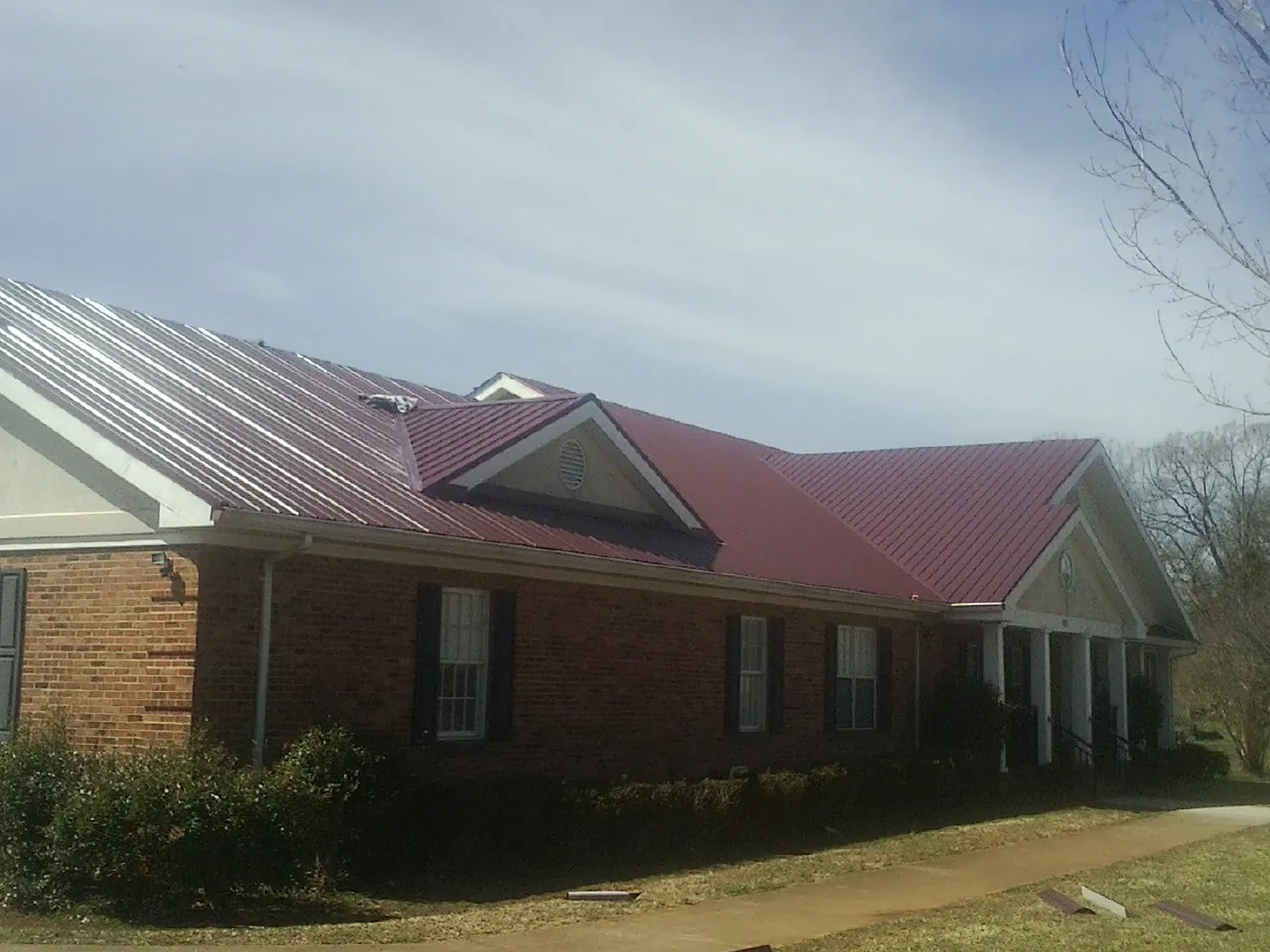 Red metal roof with gabled entries on a long brick building, from a Hail Damage Roof Repair job in Brick
