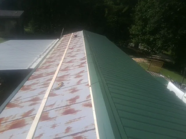 Old rusted panels beside newly installed green metal roofing — Wind Damage Roof Repair by Roofing Brothers in Brick