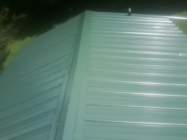 New green metal panels meeting at the ridge of a roof — Flat Roof Repair work by our crew in Brick