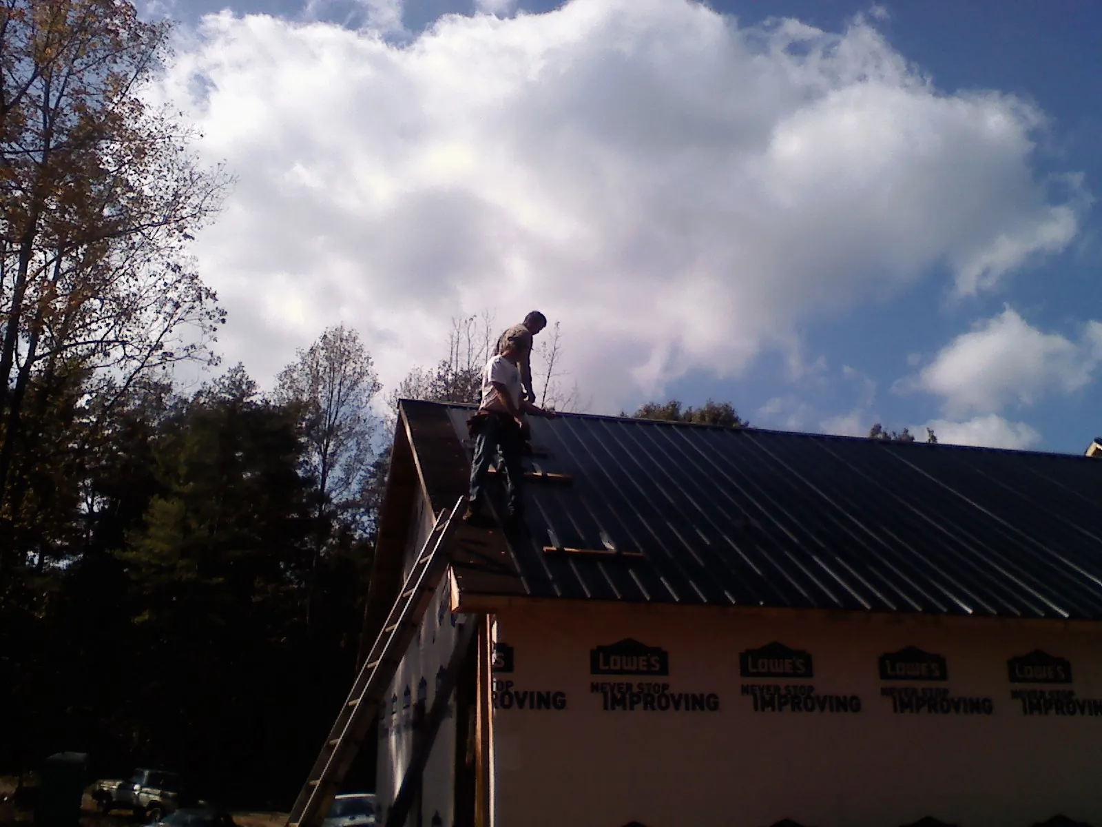 Roofer fastening dark metal panels high against a cloudy sky, from a Roof Inspection job in Brick