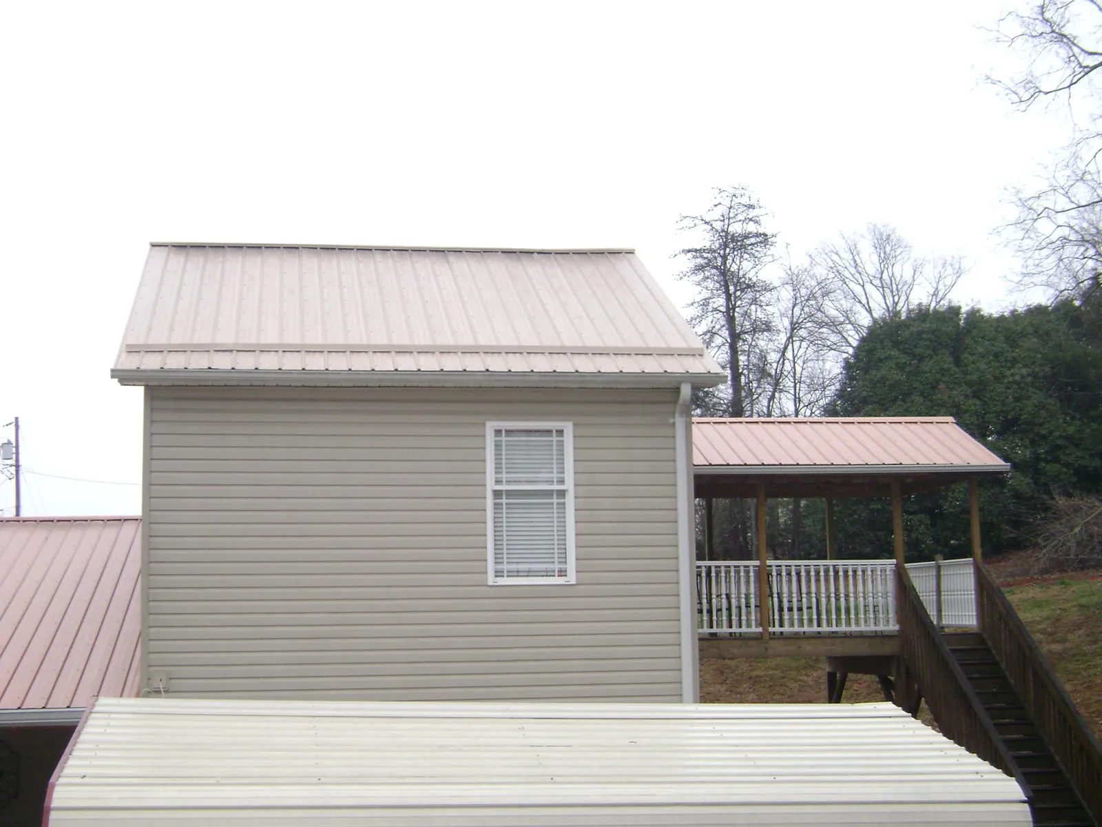 Tan metal roofs on a two story addition and attached porch, from a Roof Replacement job in Brick