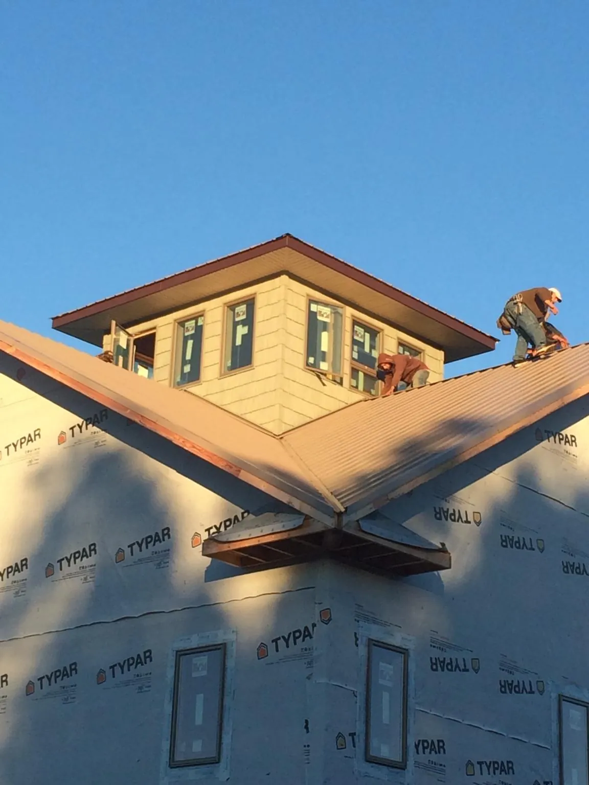 Roofers working around a rooftop cupola on a new metal roof at sunset — Roof Waterproofing in Brick by Roofing Brothers